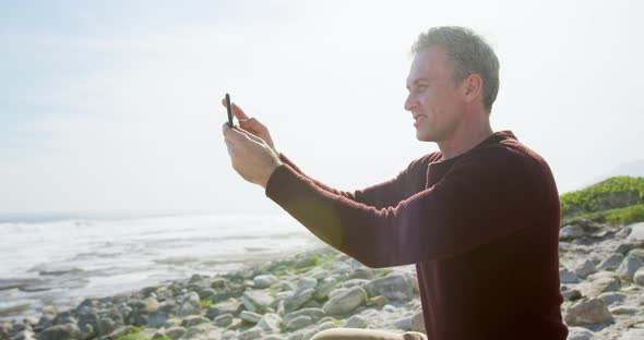 Caucasian man enjoying free time by sea on sunny day sitting on smartphone alt