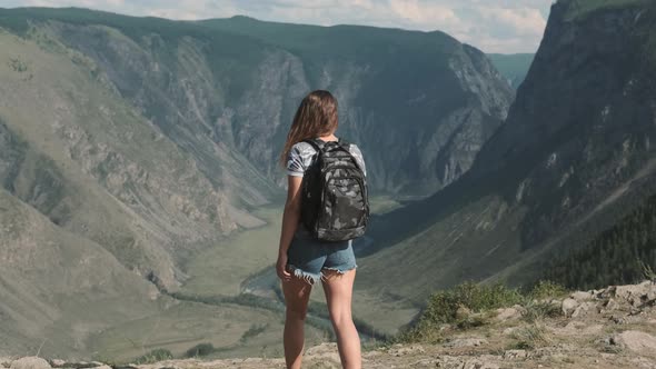 A Female Traveler with a Rucksack Climbs To the Top of the Mountain and Raises His Hands Up Feeling alt