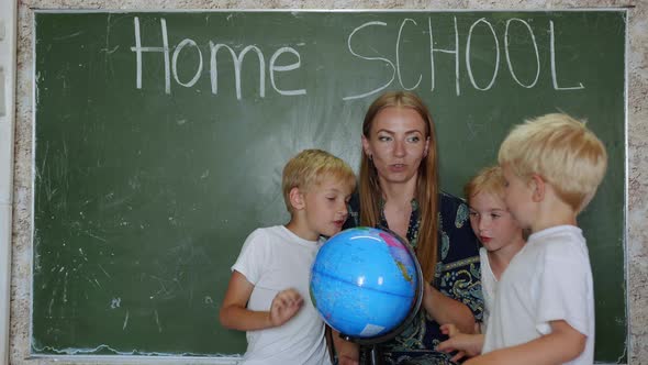 Home School Concept. A Mother Gives Her Children a Geography Lesson with a Globe in Her Hands. alt