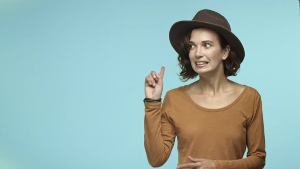 Young Woman with Curly Hair Wearing Hipster Hat Pointing Fingers Left at Copy Space for Logo or