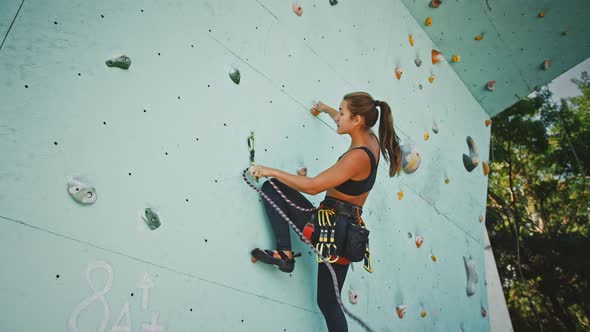 Active Woman Practicing Rock Climbing on Artificial Rock Wall in Climbing Gym Below View alt