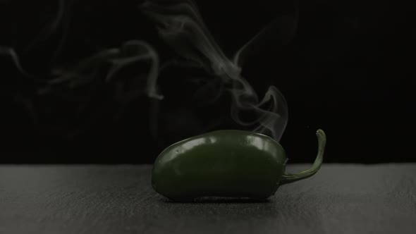 Green jalapeño chili pepper with smoke effect on black background