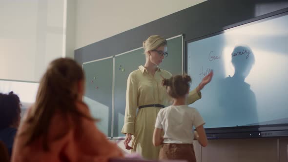 Young Schoolteacher and Schoolgirl Standing at Smart Board in Classroom alt
