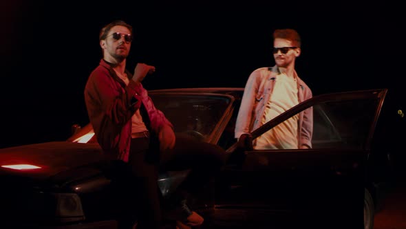 Two Men in Sunglasses Dance Vigorously Outside Car on the Street at Night