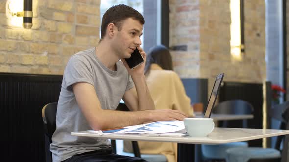 Young Millennial Successful Businessman Talking on the Phone and Typing on Laptop Keyboard alt