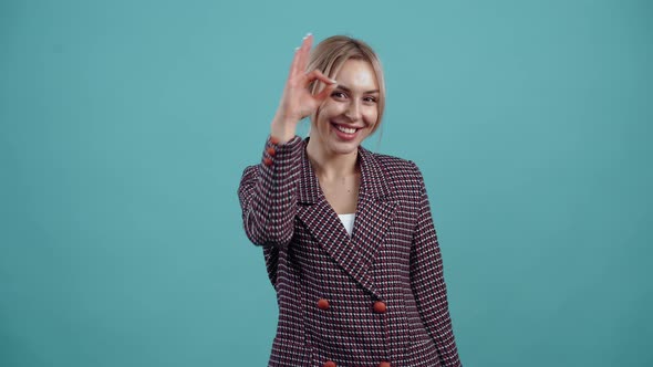 Funny Blonde Looks Happy the Ok Sign Brings It to Her Eyes and Playful Looks with Her Index Finger alt