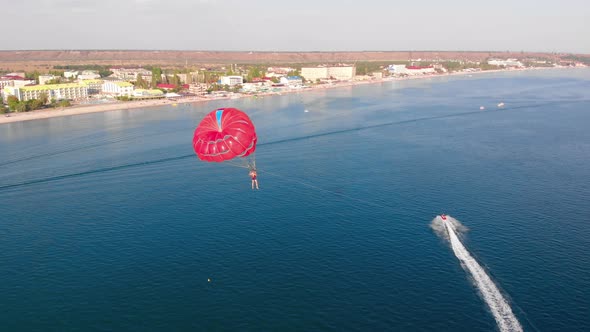 Towing Red Parachute Behind a Jetski Over the Sea Along the Beach at Sunset alt
