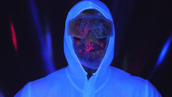 A Male in a White Luminous Suit Mask Splattered with UV Paint in the Dark alt