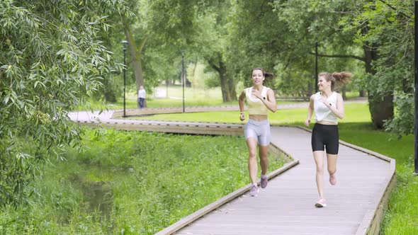 Women with Ponytails Run Along Wooden Track in Public Garden