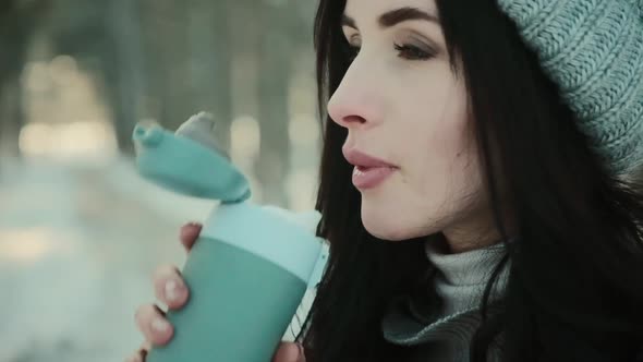 Woman in Knitted Hat Drinks Hot Beverage in Winter Forest