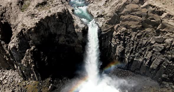 Aerial view of a crane shot of a powerful waterfall that generates a rainbow as it falls by the acti alt