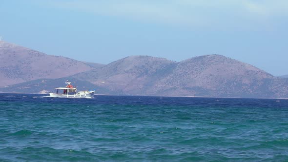 Slow motion of a fishboat set on at aegean sea, with Evia island on there background alt