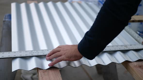 A construction worker measuring sheet metal with a straight edge ruler before cutting. alt
