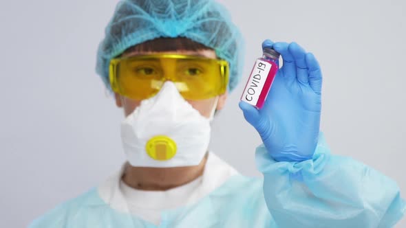 Young Scientist in Biohazard Costume Holding Tube with Coronavirus and Showing It To Camera Isolated alt