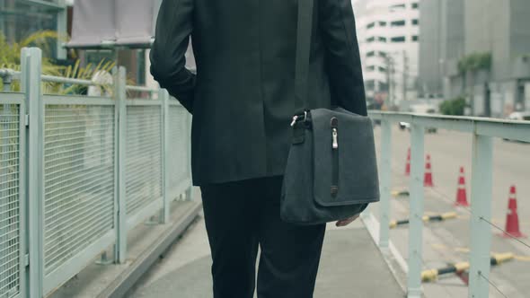 Asian businessman casual dress carrying a shoulder bag while walking in the street.