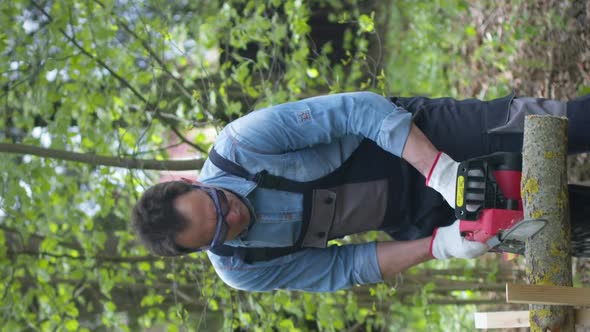 Vertical Shot Handsome Lumberjack in Working Uniform Sawing Wood with Chainsaw on Sawhorse