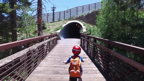 A boy rides his mountain bike through a tunnel on a paved trail in the woods. alt