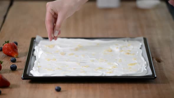 A professional pastry chef makes a meringue roll, sprinkle almonds flakes on the base alt