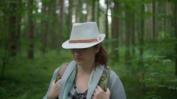 Woman in a Hat and with a Backpack Walks Through the Forest Close Up