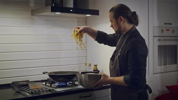 A Man in an Apron Prepares Noodles in a Wok at Home alt