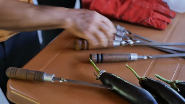 a Male Cook in a National Restaurant Pierces and Sticks Whole Black Eggplants on Sharp Metal Skewers