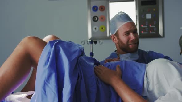 Side view of Caucasian female surgeon examining pregnant woman during labor in operation theater at alt