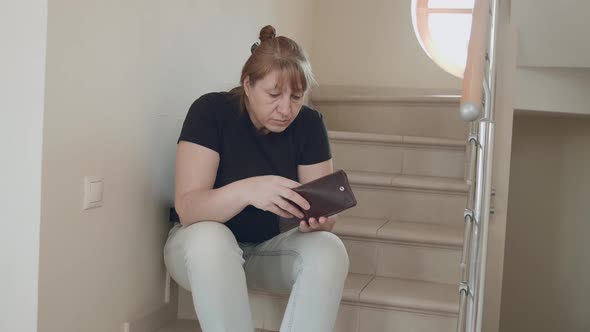 A Caucasian woman is sitting on the stairs and cannot find money in her wallet. alt