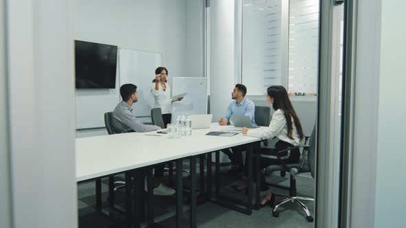 Female Business Coach Speaker Pointing on Flip Chart Presenting New Project Plan at Conference alt