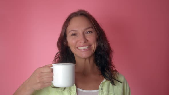 Smiling Cheerful Woman Hold Hot Cup of Coffee or Tea Isolated on a Pink Color Background alt
