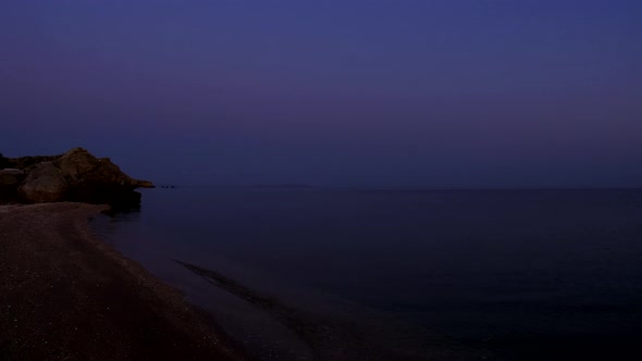 Dawn. Sea Waves Wash the Sandy Beach. A Rocky Cliff Protrudes Into the Sea. The Sky Changes Color alt