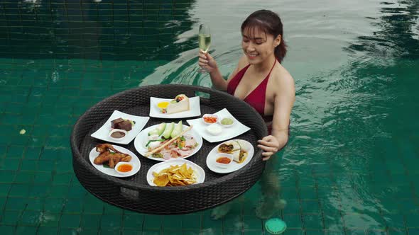 cheerful young woman enjoying with floating food and champagne glass in swimming pool
