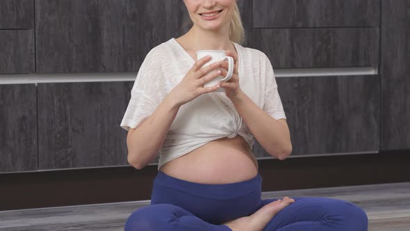 Closeup of a Pregnant Woman Drinking Water or Tea From a Cup Sitting on the Floor After Doing Yoga