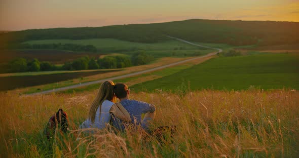 Pair of Tourists in Love Sits on a Hill and Enjoys the Sunset alt