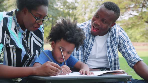 Lovely black family has a fan with son to drawing during picnic in the park