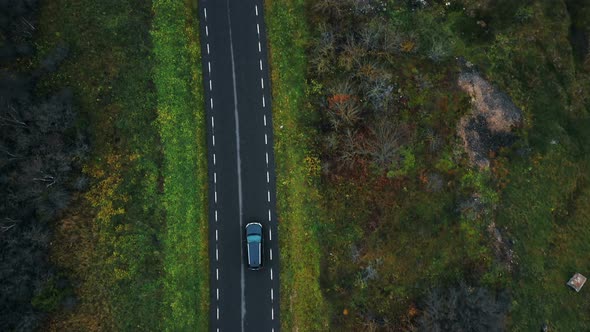 Aerial Top View, Drone Zooming in on Black Car Moving Along Highway Road Along Autumn Forest on a alt