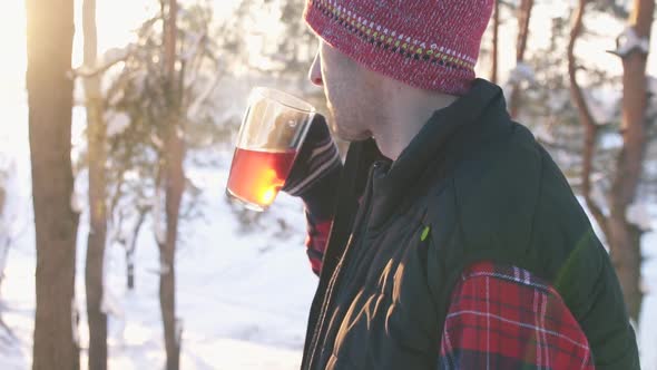 Guy in Winter Clothes Drinking Hot Mulled Wine at Sunset in Winter Forest Winter Fun alt