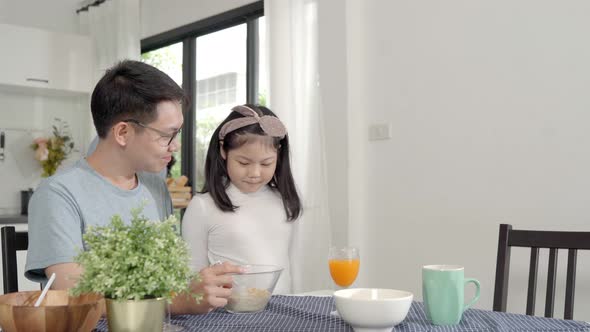 Parent and daughter eating Cereals with milk having breakfast morning in kitchen. alt