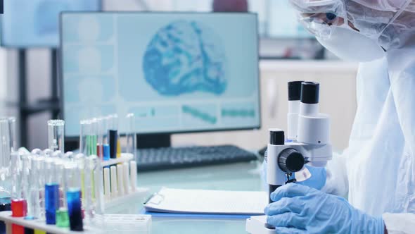 Researcher Taking Notes in Clipboard and Looking Into the Microscope