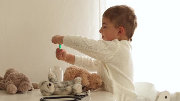 Cute little boy playing doctor at home and curing plush toy