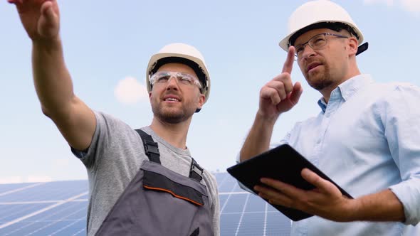 Two Workers in Helmets Check the Installed Solar Panels alt