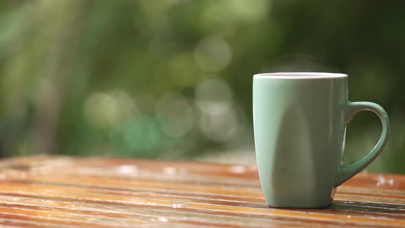 Hot coffee cup with smoke on wood table in blur green nature background with copy space
