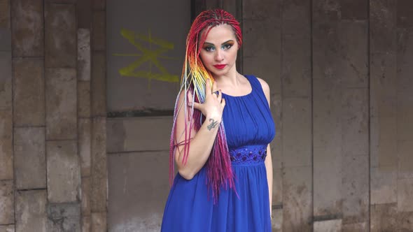 A Funny Girl with Bright Makeup and Colored Braids in a Light Blue Dress is Spinning and Laughing alt