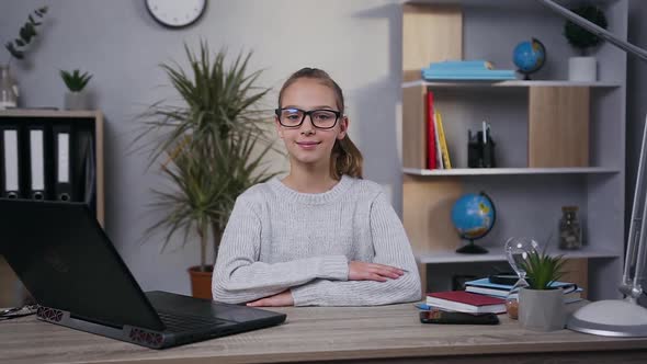 Smiling Modern Teen Girl in Glasses Sitting at Her Workplace at Home and Posing on Camera alt