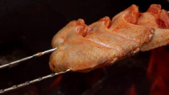 The Raw Marinated Chicken Wings on the Skewers are Placed Above the Open Fire alt