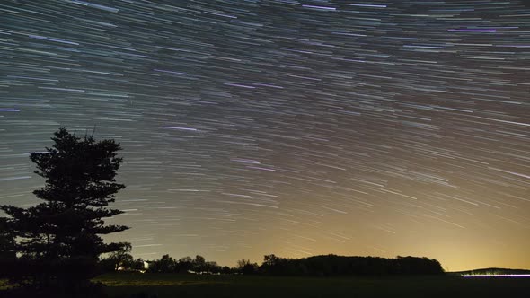 startrails over rural landscape with field in front of forest sihlouette alt