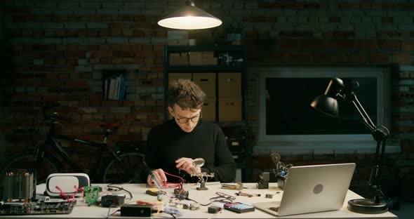 Man Solders Electronic Circuit in Loft Workshop or Startup Office at Night