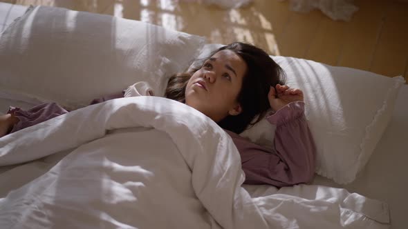 Exhausted Sad Little Woman Lying in Bed Looking Up Covering with Duvet alt