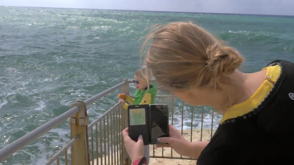 Mom taking cell photo of child looking at sea Rosh Hanikra alt