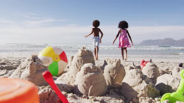 African american brother and sister running towards the sea on the beach alt