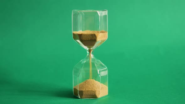 Hourglass on Green Background. Sand Is Pouring From One Part To Another. Time and Transience Concept alt